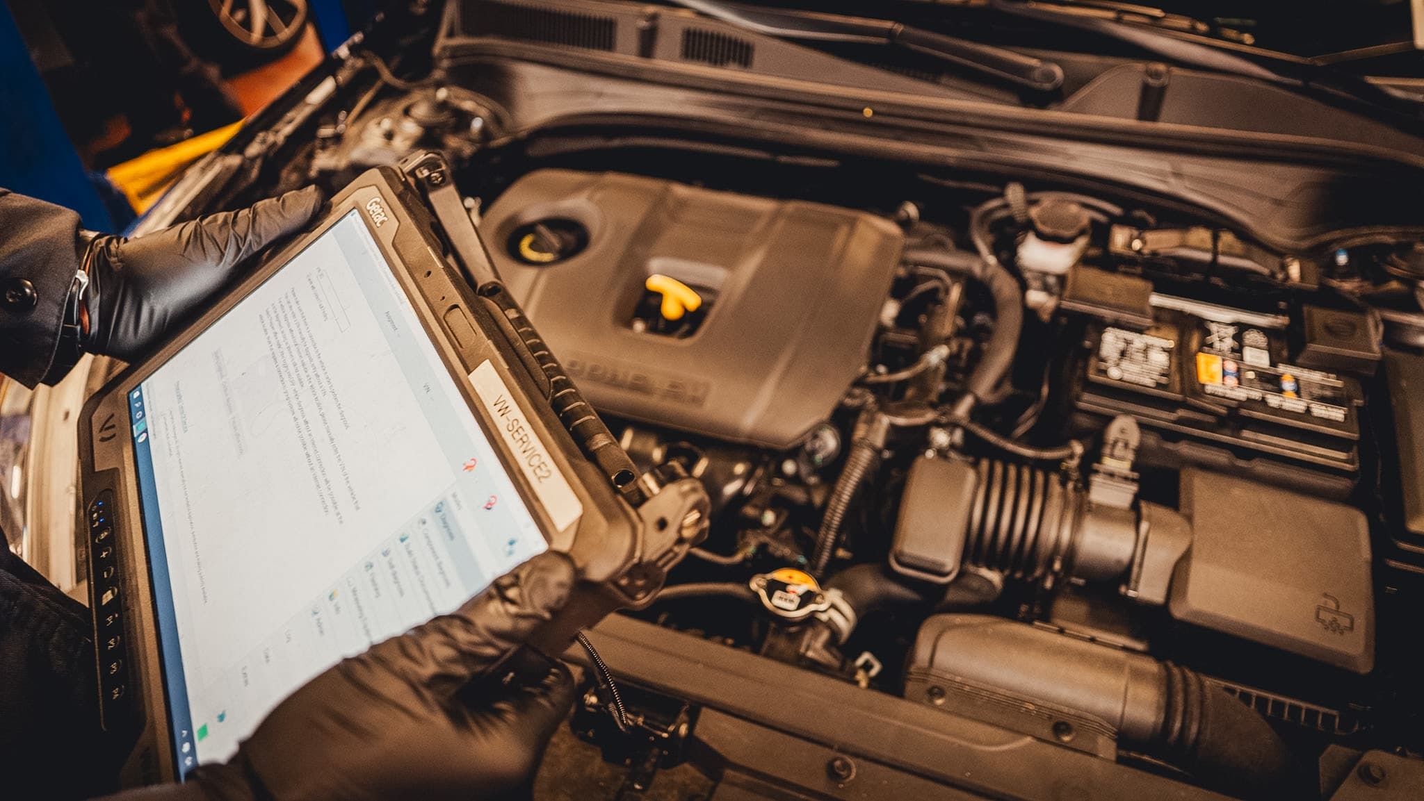 Technician using a diagnostic tablet while inspecting an engine bay.